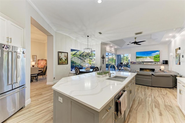 kitchen featuring light stone counters, high quality fridge, ceiling fan, a kitchen island with sink, and pendant lighting