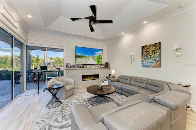 living room with ceiling fan, a raised ceiling, light hardwood / wood-style flooring, and a brick fireplace