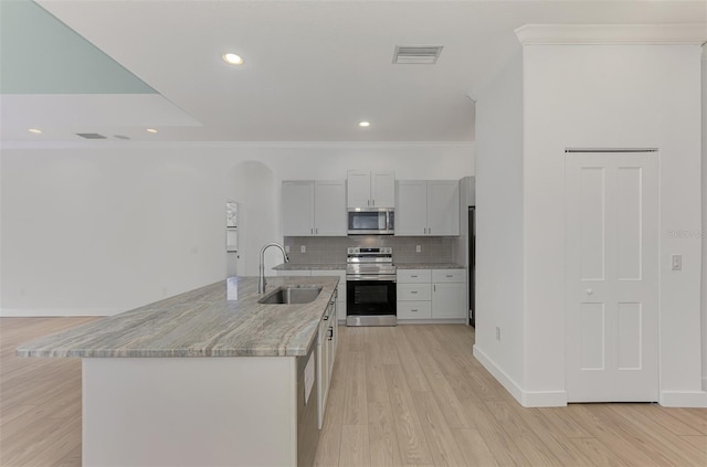 kitchen featuring sink, a kitchen island with sink, backsplash, stainless steel appliances, and light stone countertops