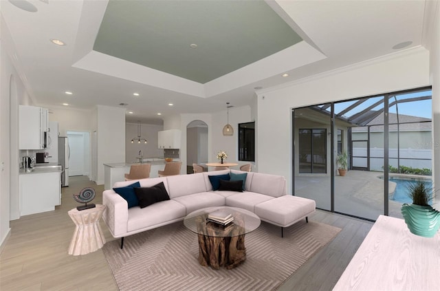 living room featuring a raised ceiling, crown molding, sink, and light hardwood / wood-style flooring