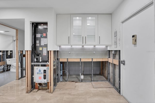 interior space with glass insert cabinets, white cabinets, backsplash, and light countertops