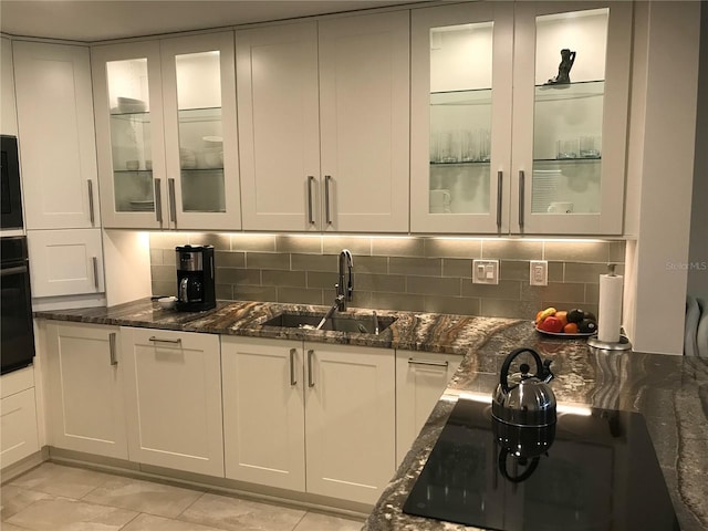 kitchen with tasteful backsplash, dark stone counters, a sink, and black appliances