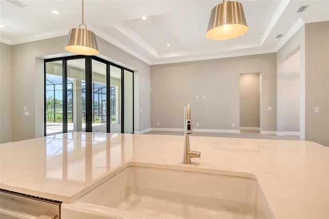 10612 Nicklaus Ct, Englewood, FL 34223 - kitchen with light stone counters, a sink, crown molding, a raised ceiling, and decorative light fixtures