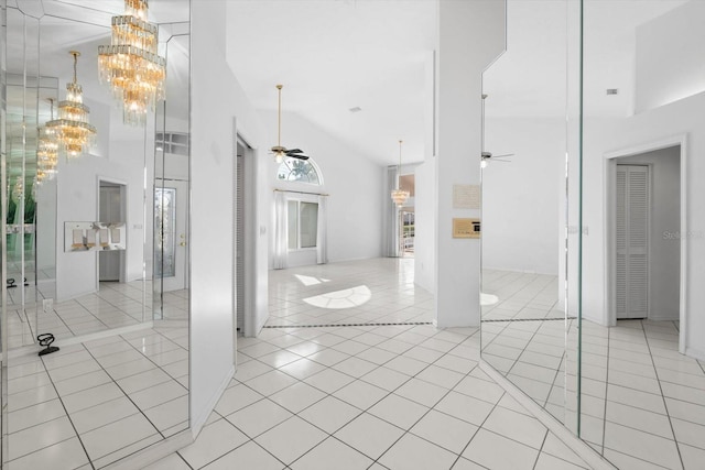 tiled empty room with ceiling fan with notable chandelier and high vaulted ceiling