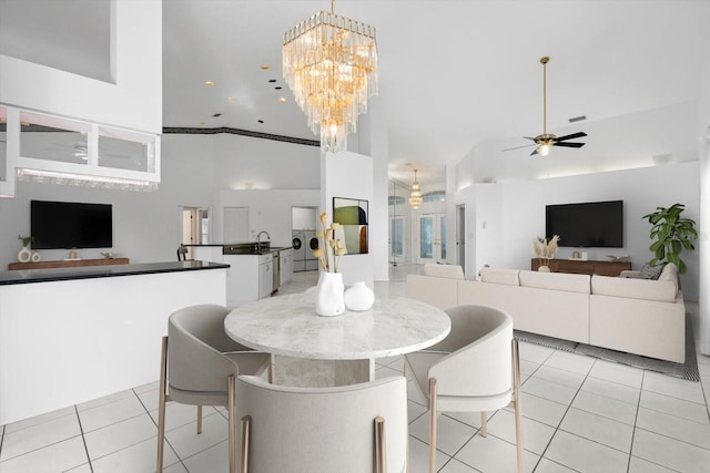 tiled dining area with ceiling fan with notable chandelier, washer / dryer, sink, and high vaulted ceiling