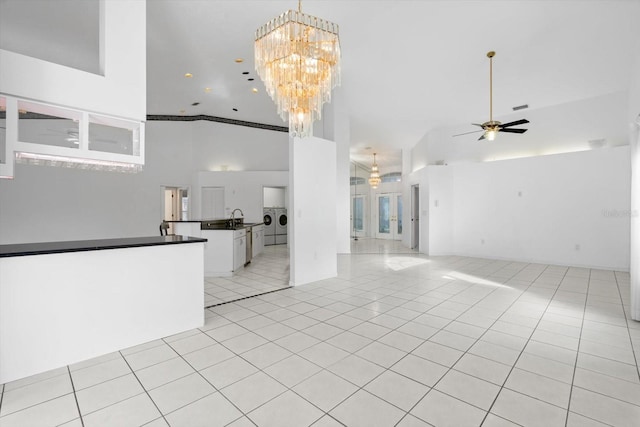 unfurnished living room featuring sink, high vaulted ceiling, light tile patterned floors, washer and dryer, and ceiling fan with notable chandelier