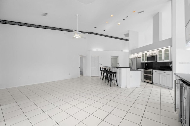 kitchen with backsplash, a kitchen breakfast bar, ceiling fan, white cabinetry, and stainless steel appliances