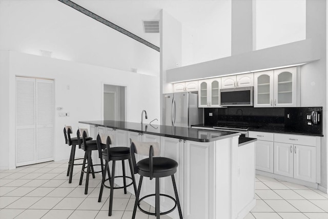 kitchen with stainless steel appliances, light tile patterned floors, a towering ceiling, a breakfast bar, and white cabinets