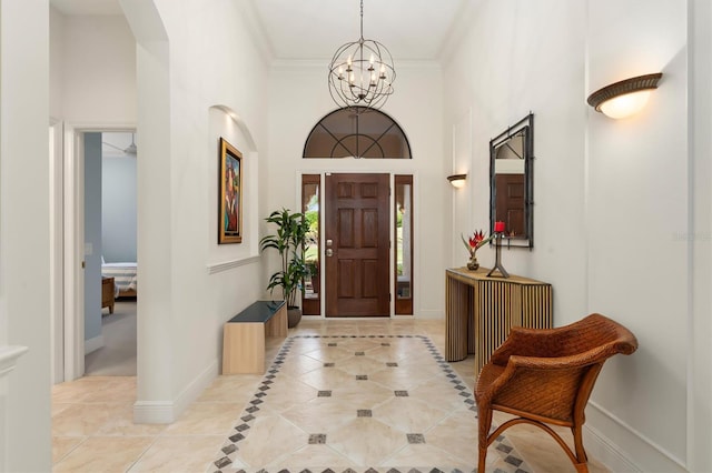 tiled entrance foyer featuring ornamental molding, a towering ceiling, and a chandelier