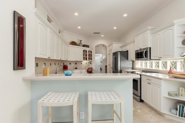 kitchen with kitchen peninsula, appliances with stainless steel finishes, a kitchen bar, and white cabinets