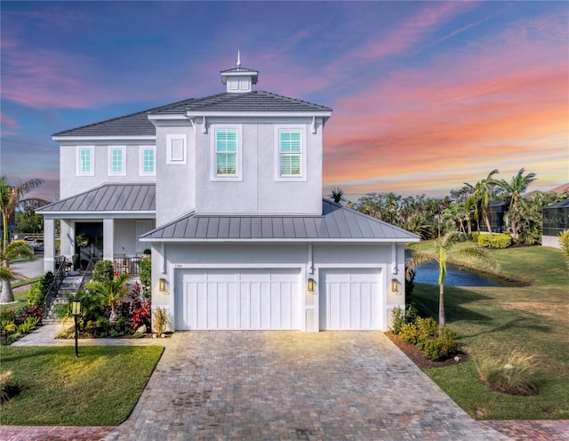 view of front of home with decorative driveway, stucco siding, a front yard, a standing seam roof, and metal roof