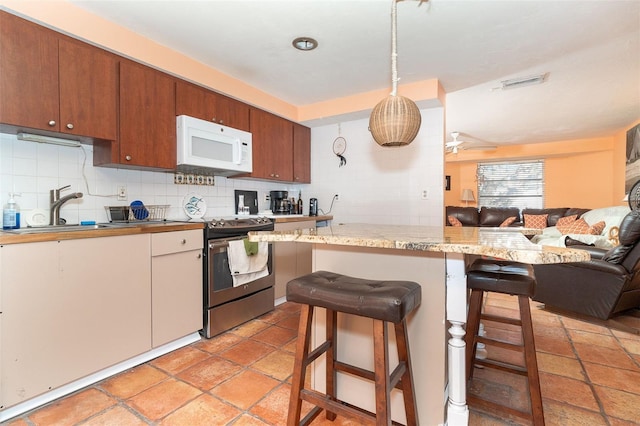 kitchen with stainless steel range with electric cooktop, a kitchen breakfast bar, sink, hanging light fixtures, and ceiling fan