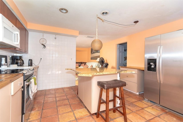 kitchen with stainless steel appliances, a kitchen breakfast bar, kitchen peninsula, decorative backsplash, and tile walls