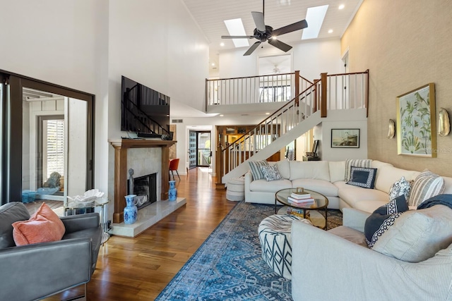 living room with a skylight, ceiling fan, dark wood-type flooring, a high ceiling, and a tiled fireplace