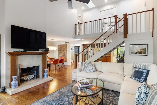 living room featuring a skylight, ceiling fan, a high ceiling, wood-type flooring, and a fireplace