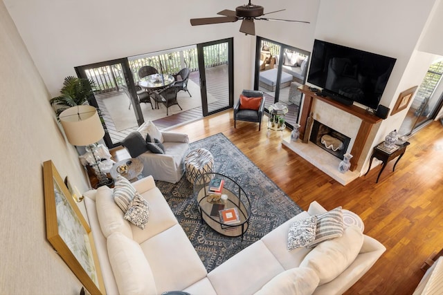 living room featuring hardwood / wood-style floors, ceiling fan, a high ceiling, and a tiled fireplace