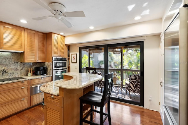 kitchen featuring ceiling fan, a center island, stainless steel appliances, decorative backsplash, and a breakfast bar