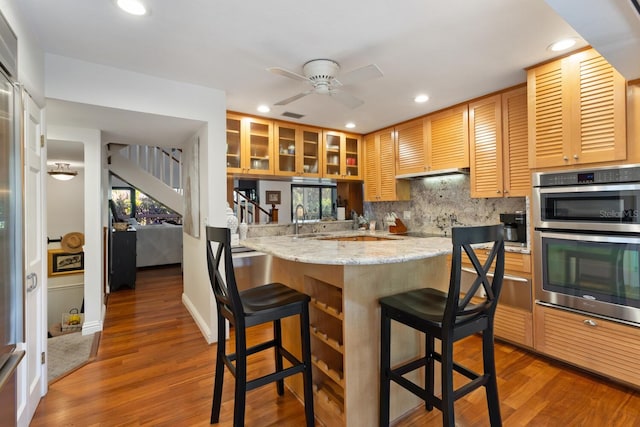 kitchen with double oven, kitchen peninsula, a kitchen bar, and dark hardwood / wood-style floors