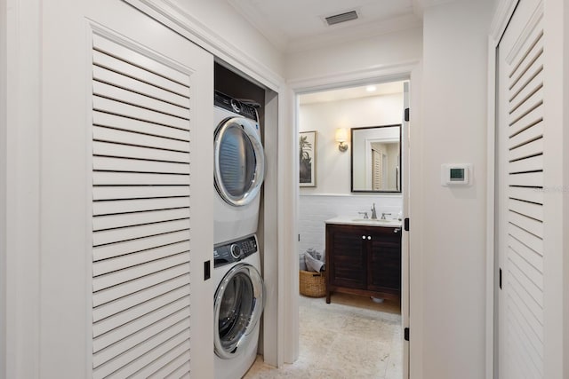 laundry room with crown molding, stacked washer and clothes dryer, and sink