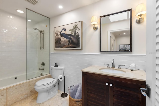 full bathroom featuring tiled shower / bath combo, toilet, tile walls, and vanity