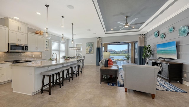 kitchen featuring a center island with sink, a kitchen bar, ornamental molding, and a tray ceiling