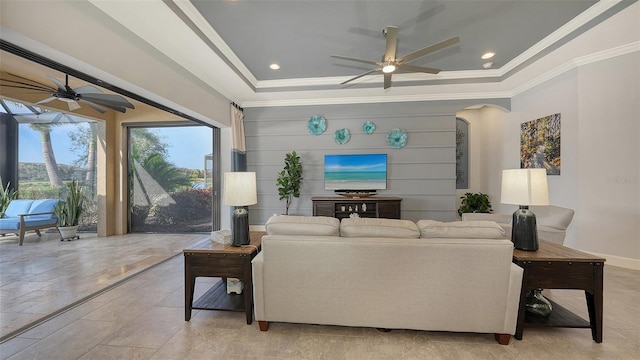 living room featuring ceiling fan, ornamental molding, and a tray ceiling