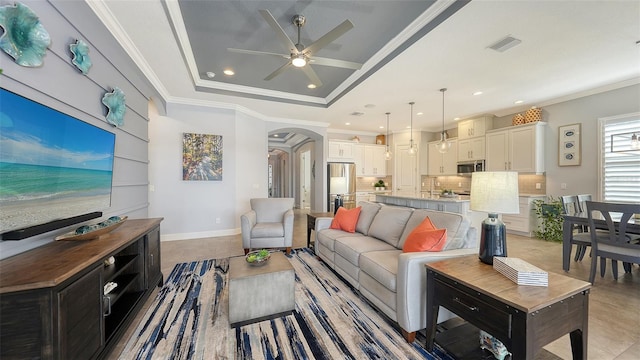 living room featuring a raised ceiling, ceiling fan, sink, and ornamental molding