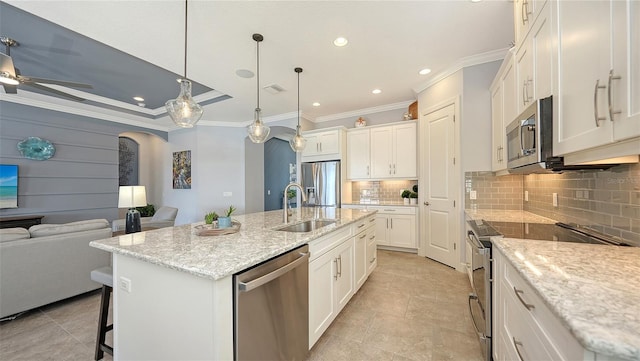 kitchen with light stone countertops, stainless steel appliances, white cabinets, hanging light fixtures, and an island with sink