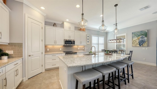 kitchen with decorative backsplash, stainless steel appliances, a kitchen island with sink, decorative light fixtures, and white cabinets