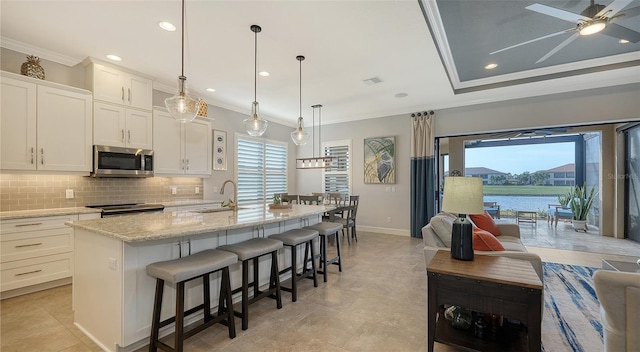 kitchen with ornamental molding, a kitchen island with sink, sink, white cabinets, and hanging light fixtures