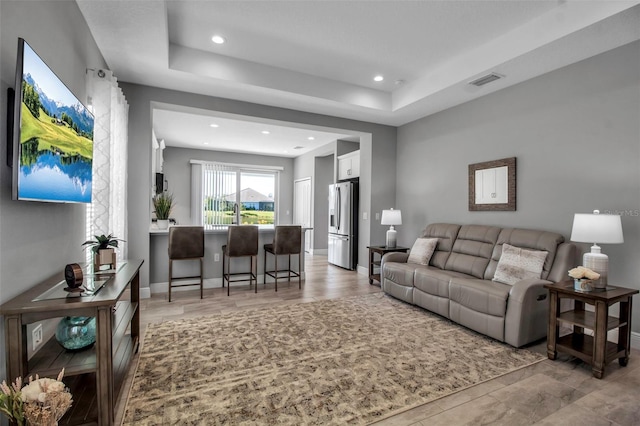 living room with light wood-type flooring and a raised ceiling