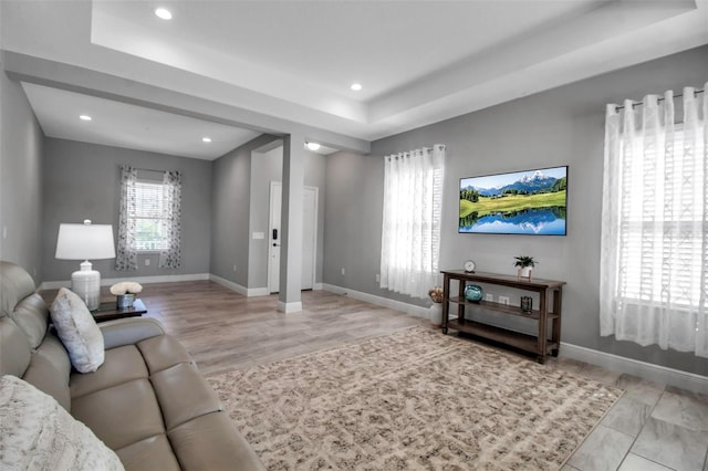 living room with a tray ceiling and light wood-type flooring