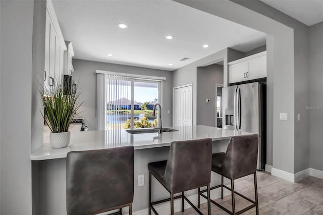 kitchen featuring sink, a kitchen breakfast bar, stainless steel refrigerator with ice dispenser, kitchen peninsula, and white cabinets