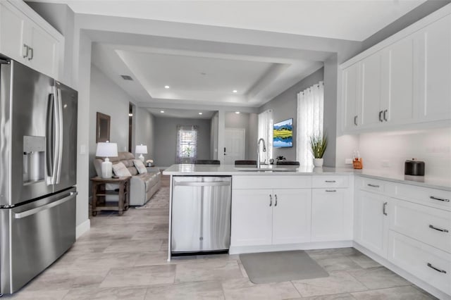 kitchen with a raised ceiling, sink, white cabinetry, kitchen peninsula, and stainless steel appliances