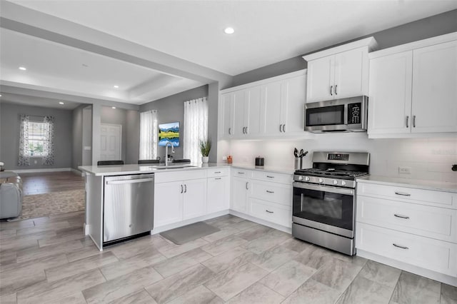 kitchen featuring sink, tasteful backsplash, kitchen peninsula, white cabinets, and appliances with stainless steel finishes