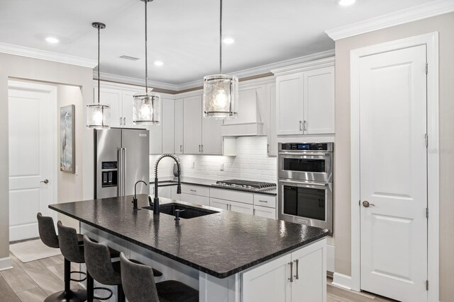 kitchen featuring a center island with sink, appliances with stainless steel finishes, hanging light fixtures, white cabinets, and sink