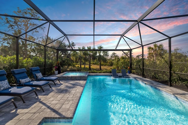 pool at dusk with an in ground hot tub, a lanai, and a patio area