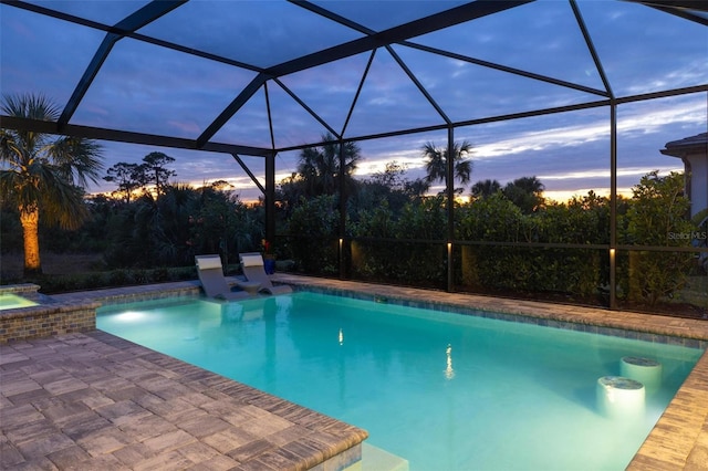 pool at dusk featuring a lanai and a patio