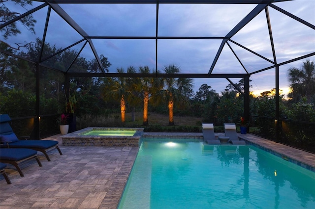 pool at dusk featuring a patio area, glass enclosure, and an in ground hot tub