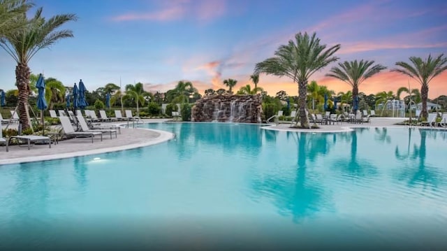 pool at dusk featuring pool water feature and a patio area