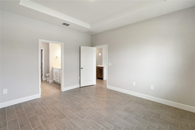 unfurnished bedroom featuring a tray ceiling and connected bathroom