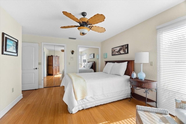 bedroom with ceiling fan, light hardwood / wood-style flooring, and multiple closets