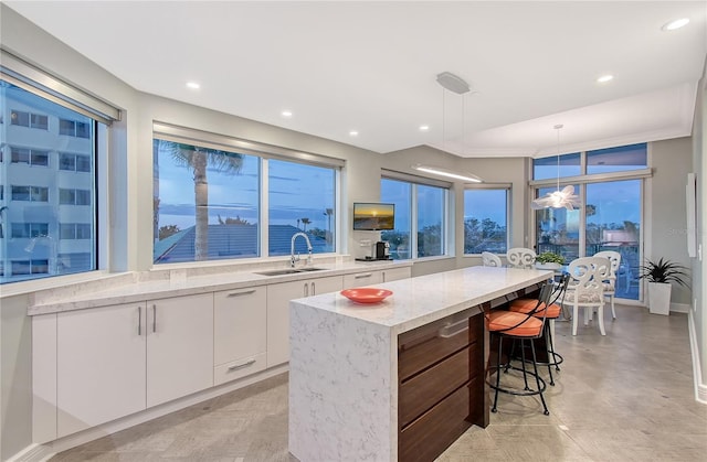 kitchen with sink, hanging light fixtures, a center island, light stone countertops, and white cabinets