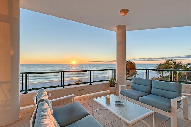 balcony at dusk featuring a water view, a beach view, and an outdoor hangout area