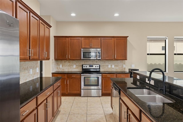 kitchen featuring backsplash, stainless steel appliances, sink, light tile patterned floors, and dark stone countertops