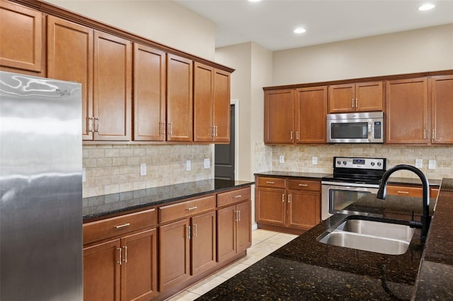 kitchen featuring light tile patterned floors, stainless steel appliances, dark stone counters, and sink