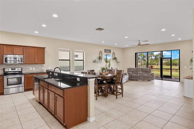 kitchen featuring appliances with stainless steel finishes, ceiling fan, sink, an island with sink, and light tile patterned flooring