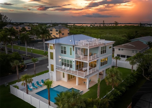 back house at dusk featuring a fenced in pool, a balcony, and a patio