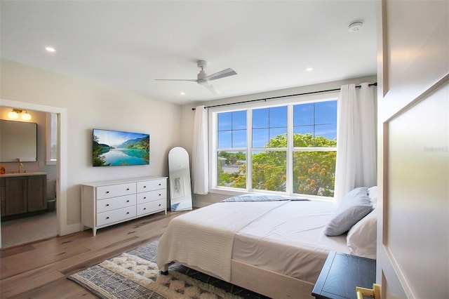 bedroom featuring hardwood / wood-style floors, ceiling fan, ensuite bathroom, and sink