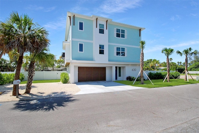 coastal inspired home featuring driveway, stucco siding, fence, a front lawn, and a garage